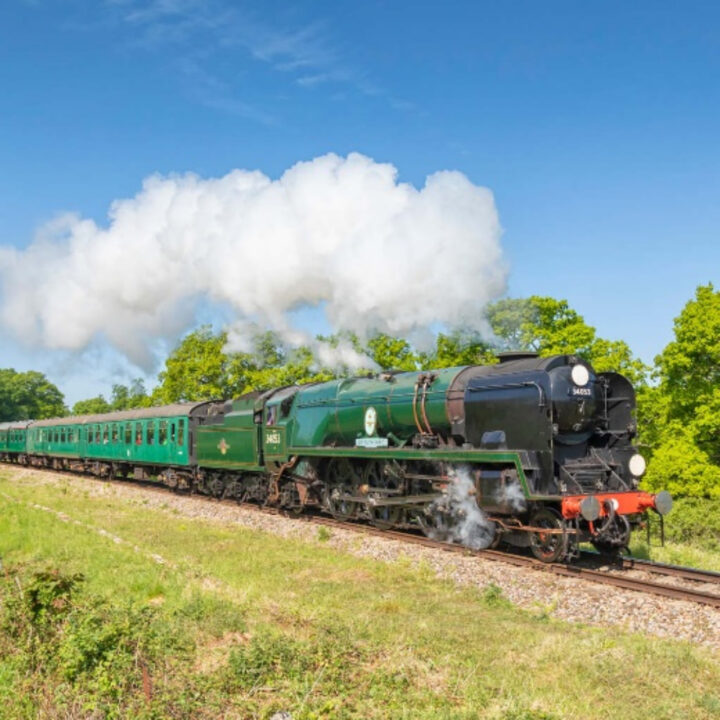 Big green steam engine pulling a passenger train.